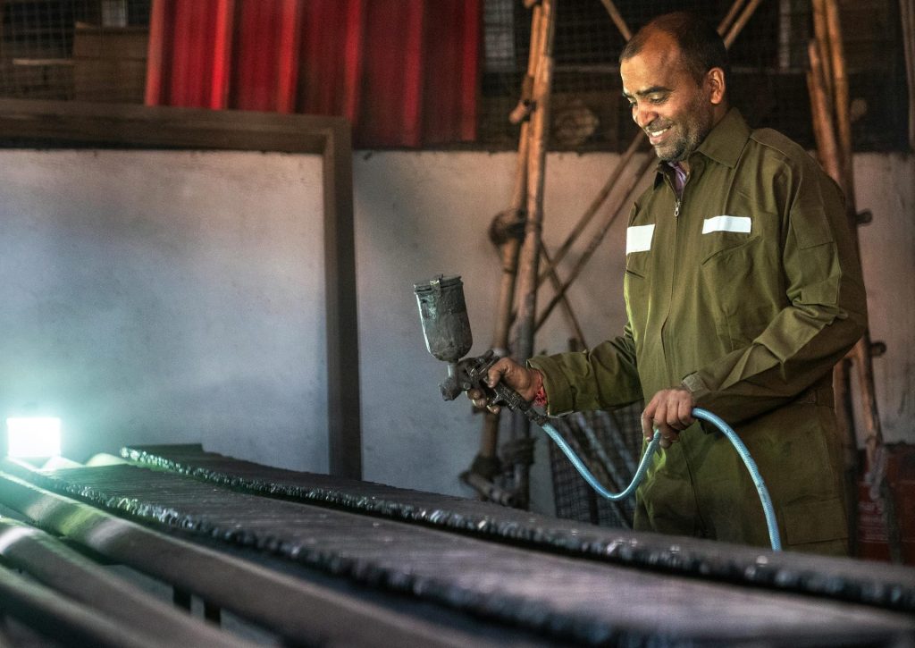 Smiling man using a paint spray gun in an industrial workshop environment.